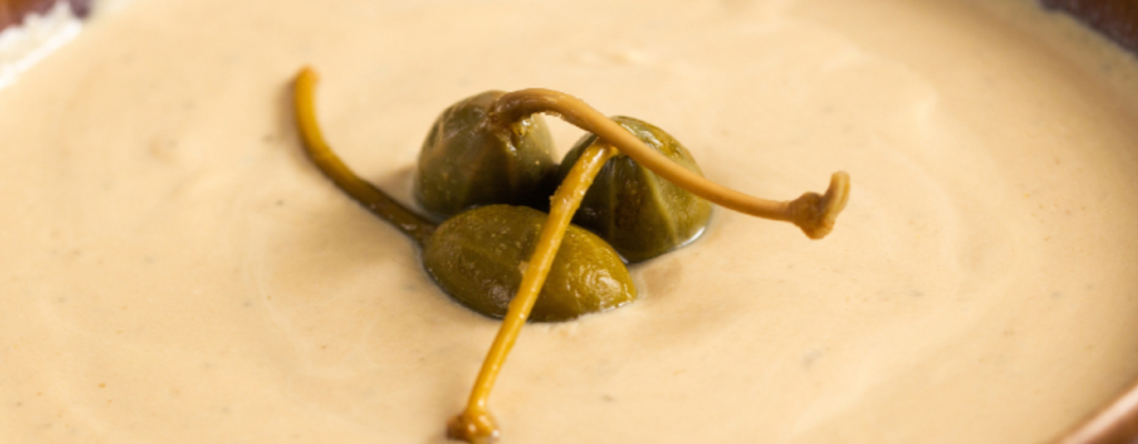 Primo piano macro di salsa tonnata con scorza di limone e capperi – texture materica e acidità visibile in dettaglio